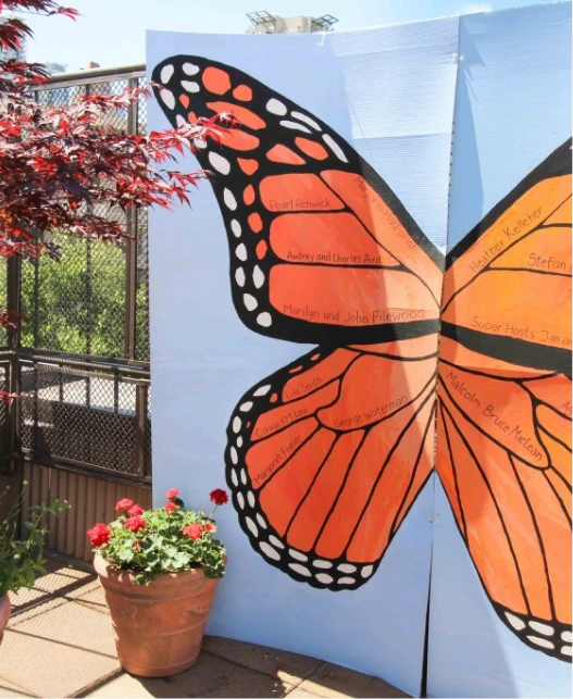 Large monarch butterfly community art installation displayed outdoors beside a potted flower plant.