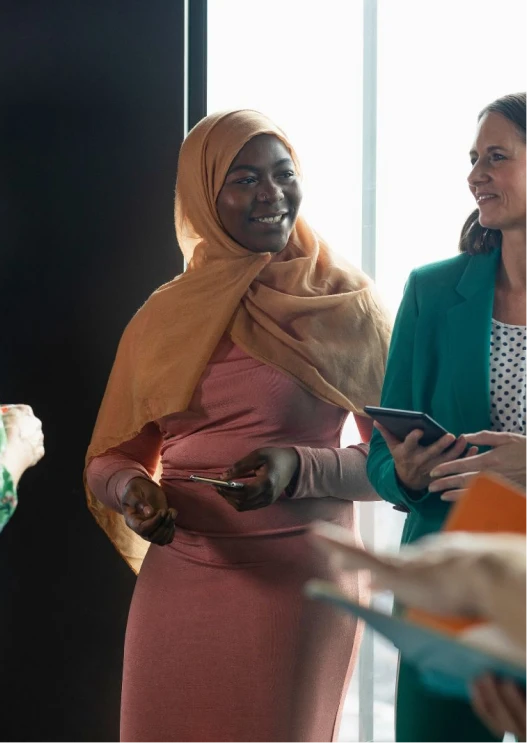 Woman wearing a headscarf and pink dress speaking with colleagues during a professional networking event indoors.
