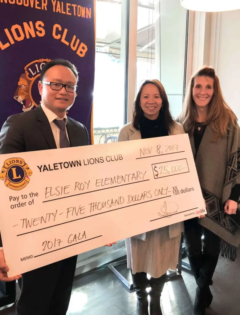 Three people holding a large donation check from Yaletown Lions Club for an elementary school fundraiser.